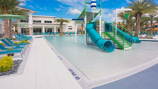 A pool area with a water slide, lounge chairs, and a building in the background. - Upstay Veranda Palms Villa Pool Hot Tub Games (Kissimmee)