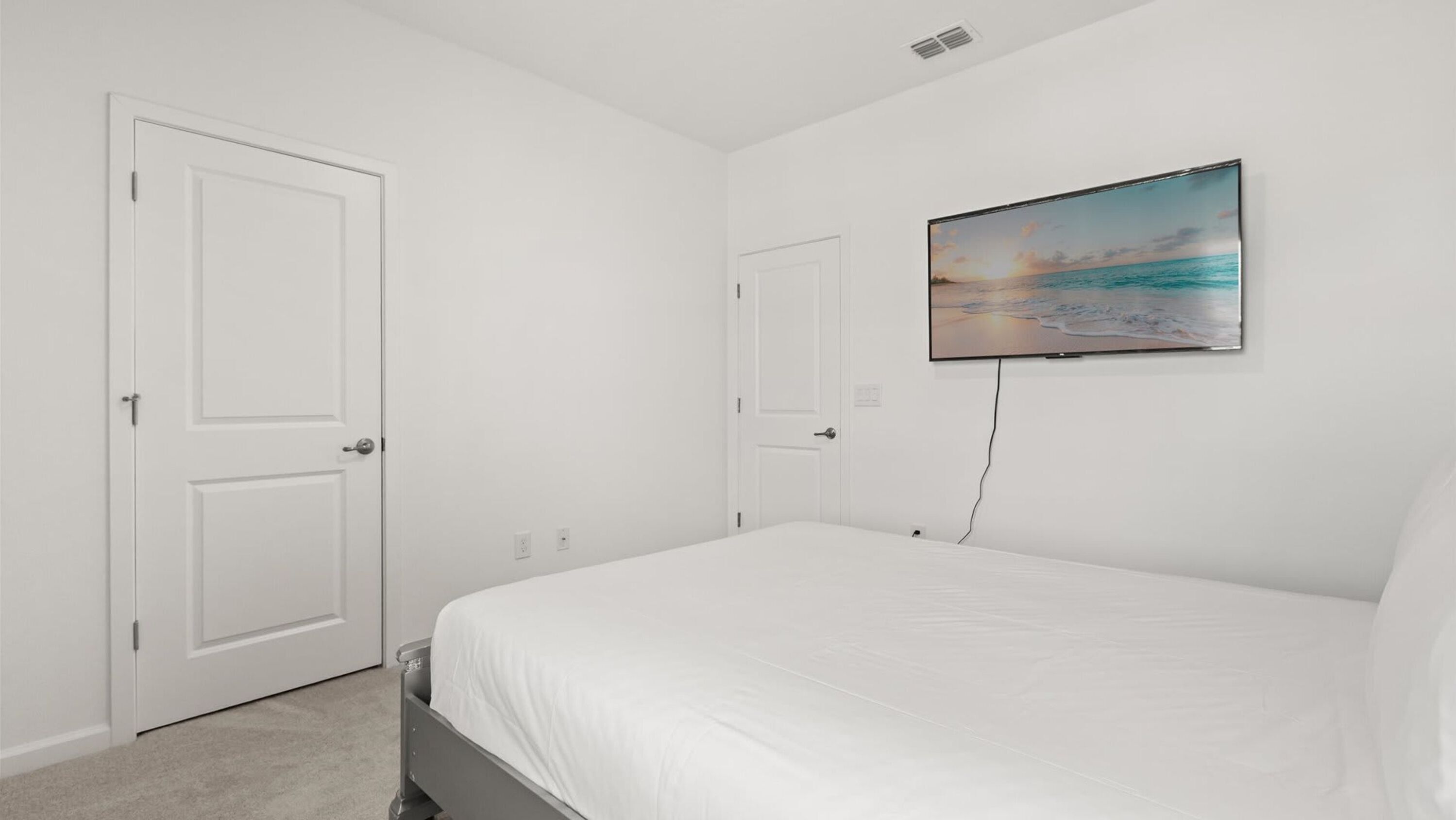 Une chambre à coucher avec un lit, un téléviseur fixé au mur et deux portes.