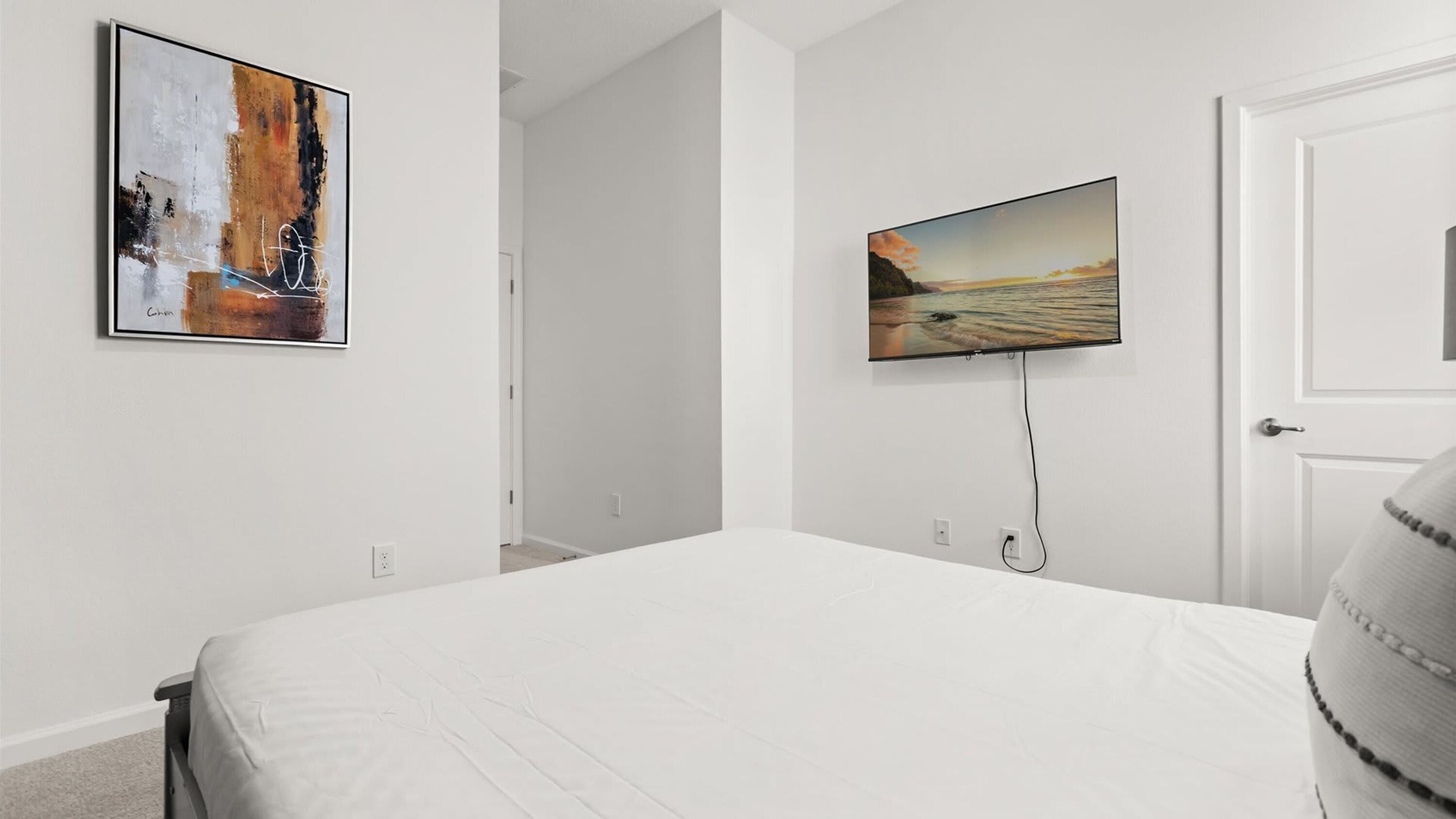 A hotel room with a large bed, a flat-screen TV mounted on the wall, and a framed abstract painting on the wall.
