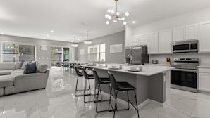 A modern kitchen with white cabinetry, stainless steel appliances, and a central island with bar stools. - Upstay Veranda Palms Villa Pool Hot Tub Games (Kissimmee)