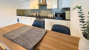 A modern kitchen with white cabinets, a black countertop, and a wooden dining table with a placemat. - 58A Thorpe Road, Norwich (Norwich)