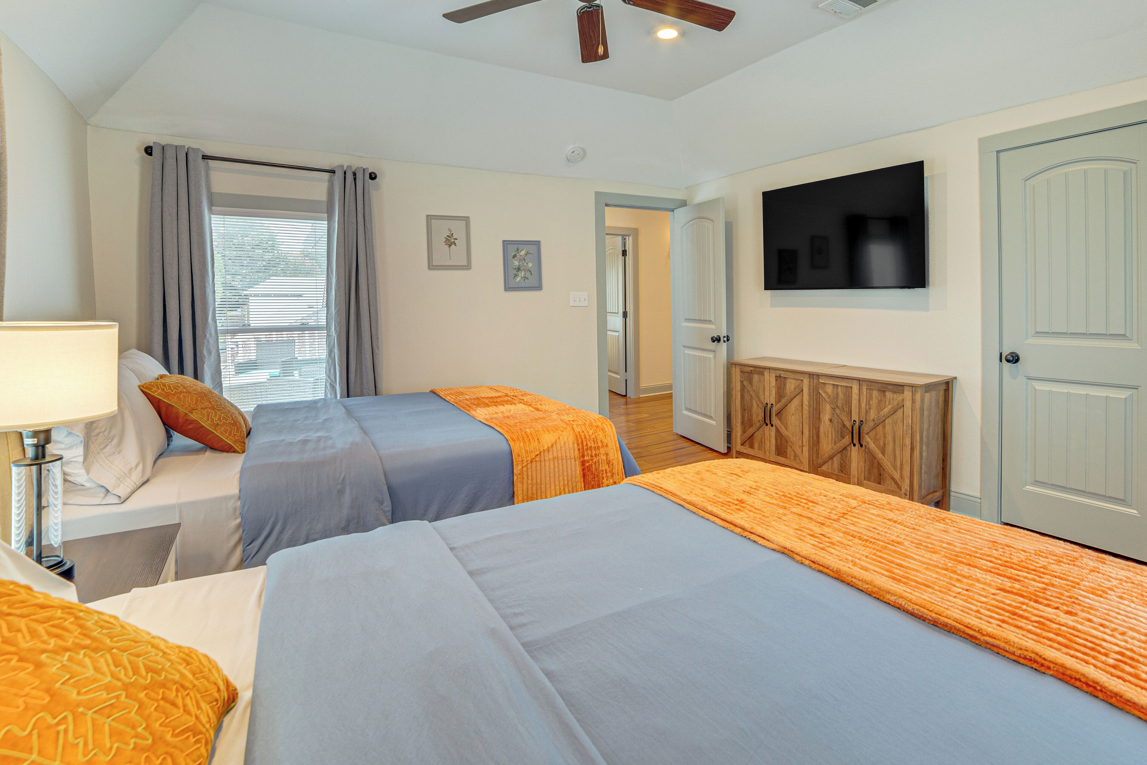 A hotel room with two beds, a TV, a ceiling fan, and a door leading to another room.