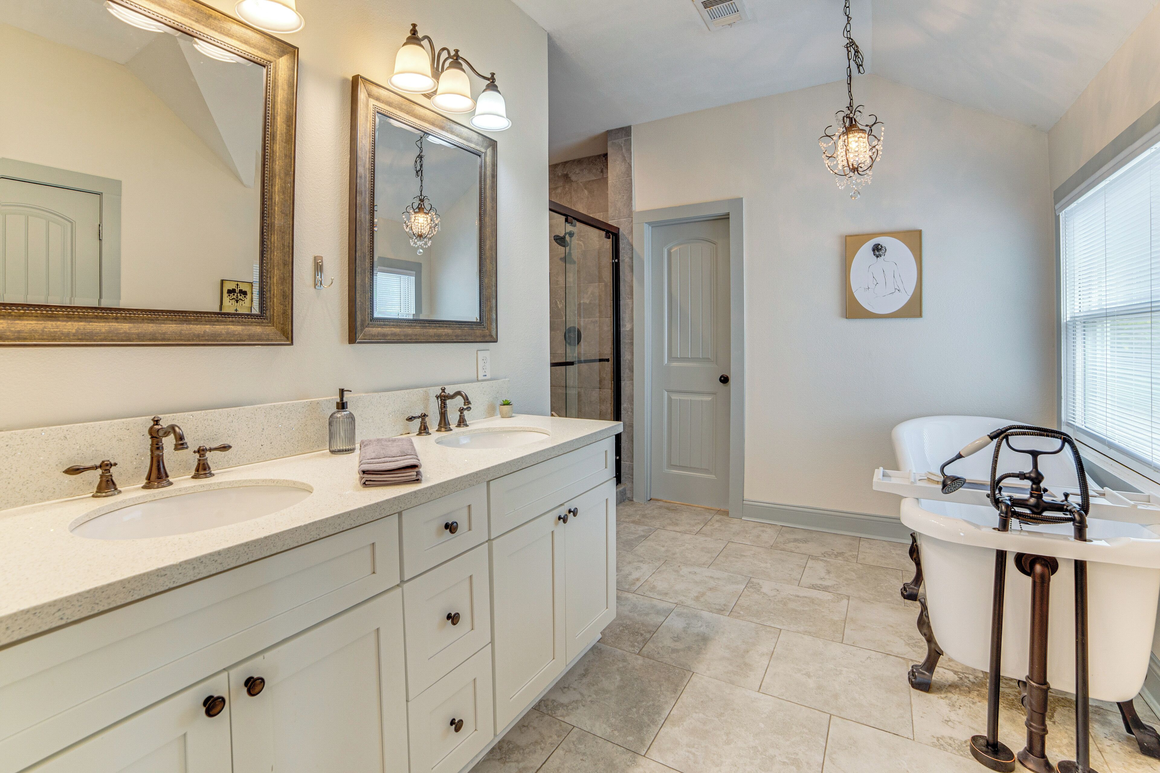 A bathroom with a double sink vanity, a bathtub with a shower head, and a large mirror with lights.