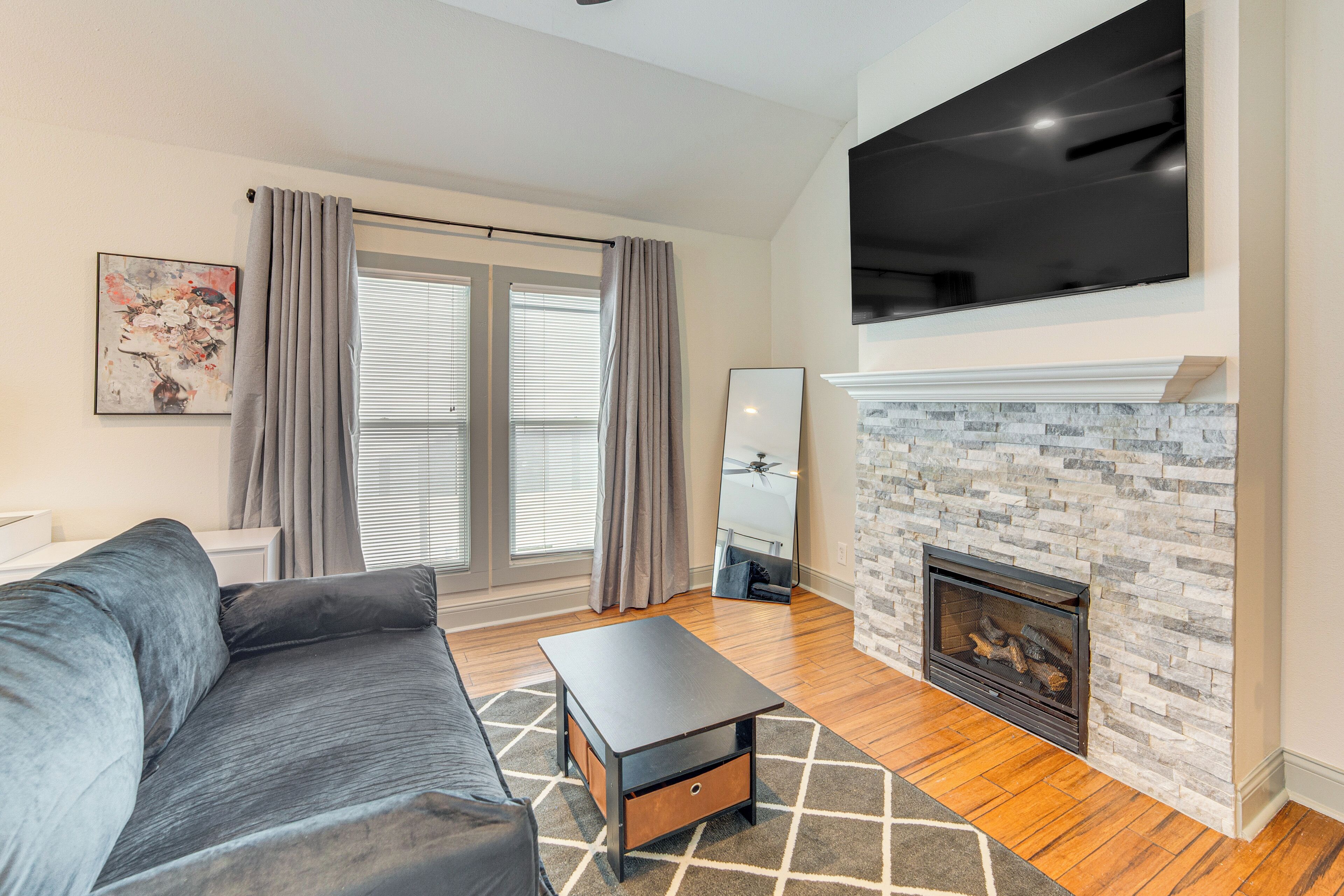 A modern living room with a grey sofa, a black coffee table, a fireplace, and a large flat-screen TV mounted above it.