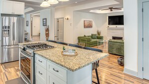 Cozinha moderna com ilha central, eletrodomésticos de aço inoxidável e área de jantar com sofá verde e lareira.