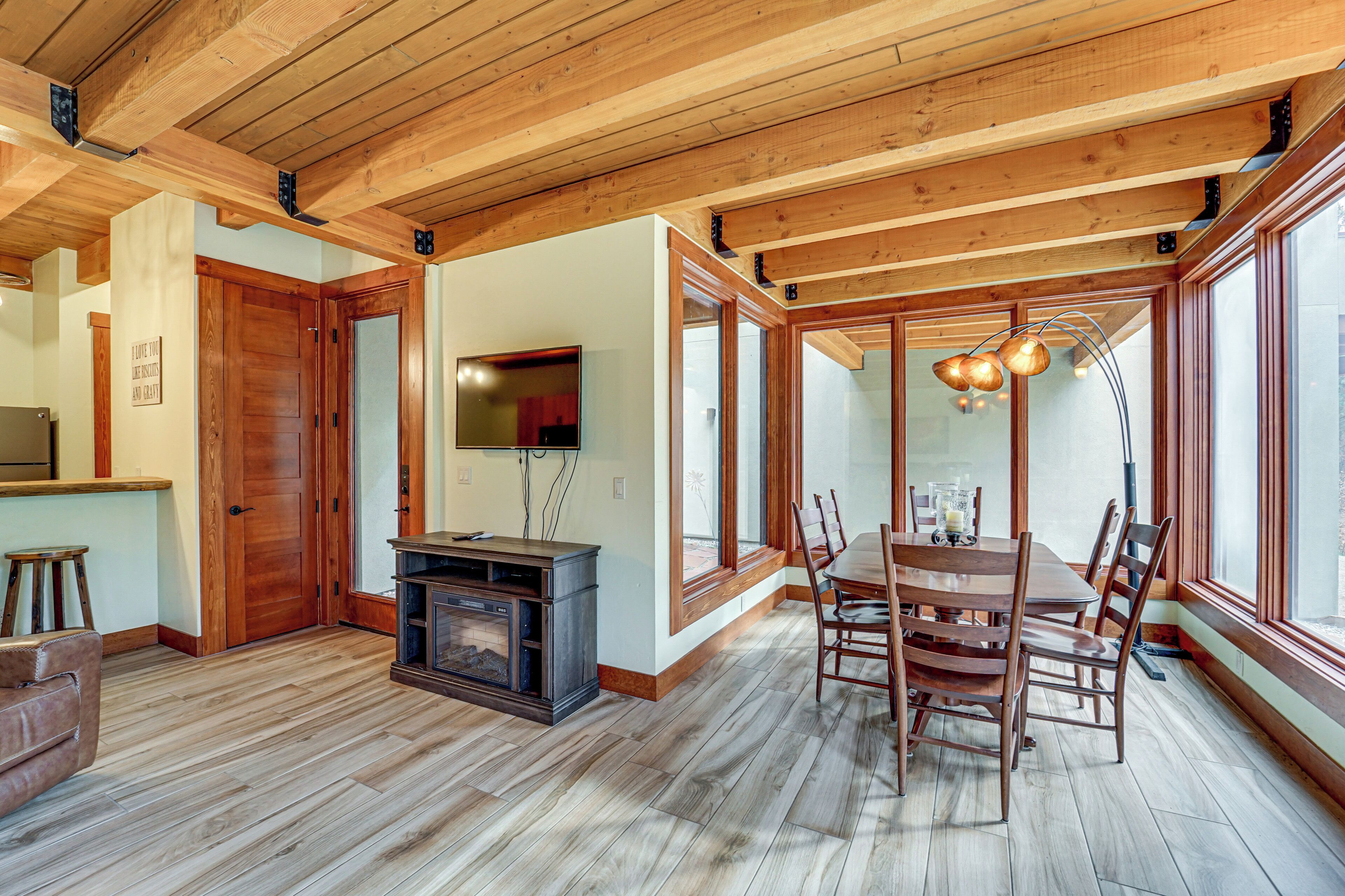 A spacious dining area with a wooden table and chairs, a built-in entertainment unit, and large windows providing natural light.