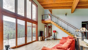 Uma sala de estar ampla com piso de madeira, um sofá vermelho, uma TV e uma escada que leva a um andar superior.