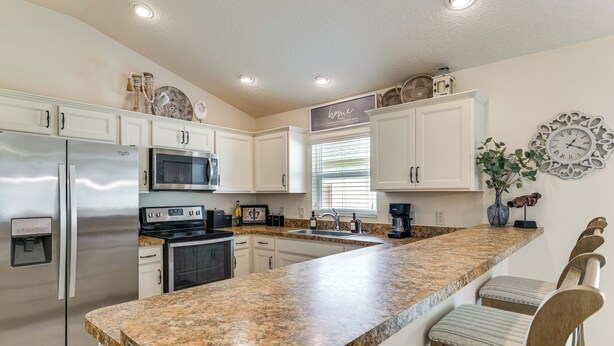 A kitchen with white cabinets, stainless steel appliances, a granite countertop, and a bar stool seating area. - Quiet Escape in The Villages! House w/ Lanai (Wildwood)