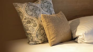Een bed met een houten hoofdbord, twee kussens met een patroon, en een effen wit kussen.