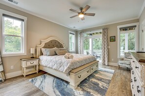 A bedroom with a bed, nightstands, a dresser, a ceiling fan, and large windows. - Explore the Seashore! Sunny Carolina Beach Home (Carolina Beach)