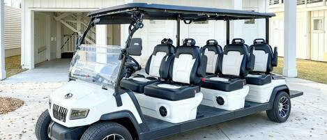 A golf cart with multiple seats parked in front of a building with a garage.