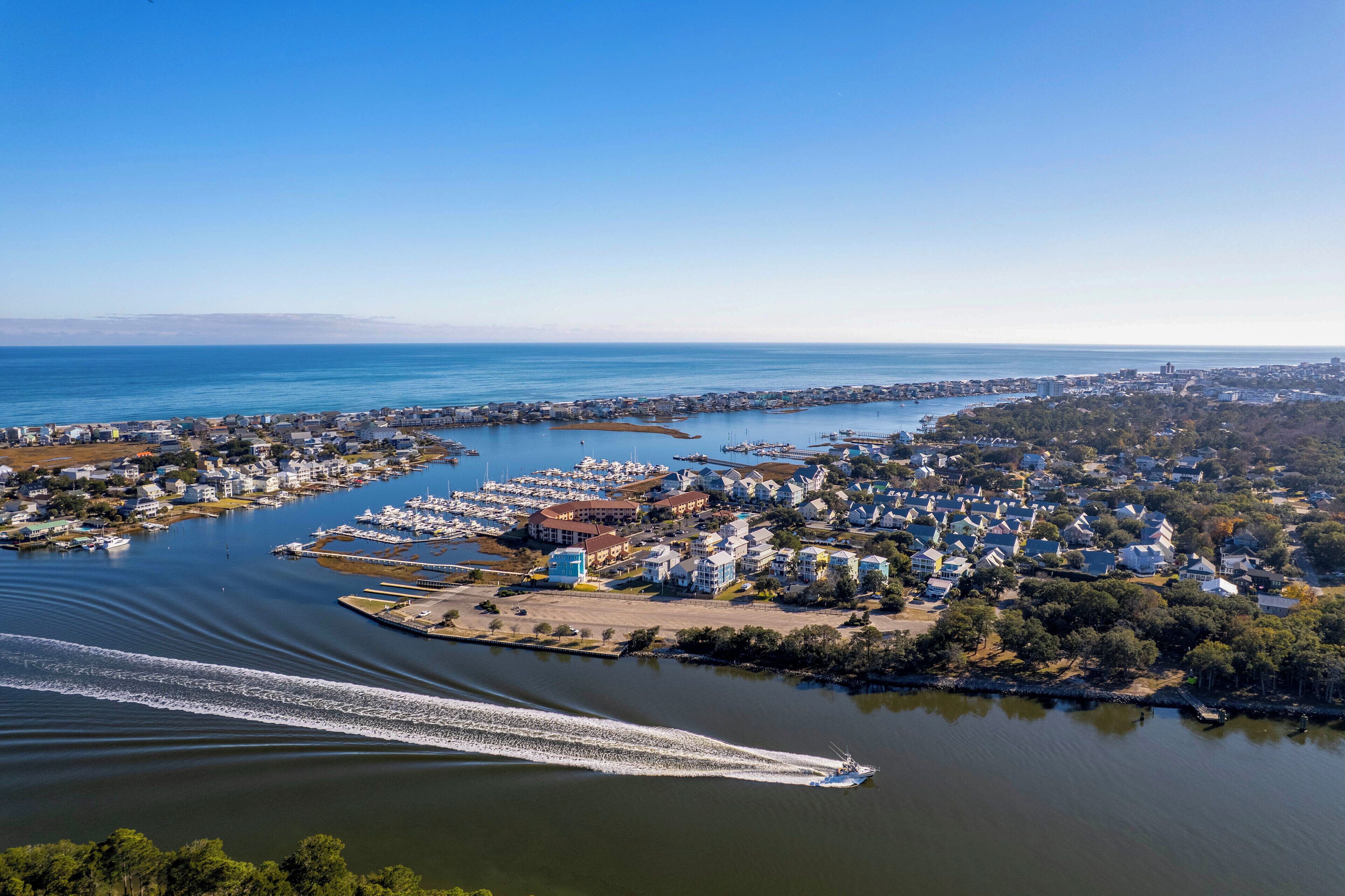 An aerial view of a coastal town with marina, residential buildings, and a boat creating a wake.