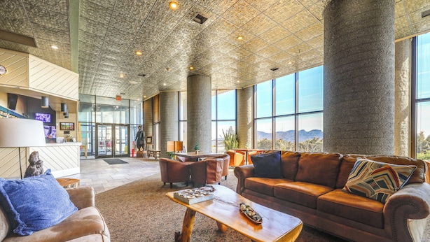 Eine geräumige Lobby mit hoher Decke, großen Fenstern und einer zentralen Sitzecke mit Sofa und Couchtisch.