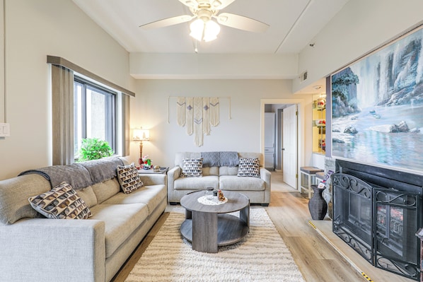 A living room with a fireplace, a sofa, a coffee table, and a painting of a waterfall. - Fun w/ Family! Sugartop Gem w/ Pool + Mtn Views (Banner Elk)
