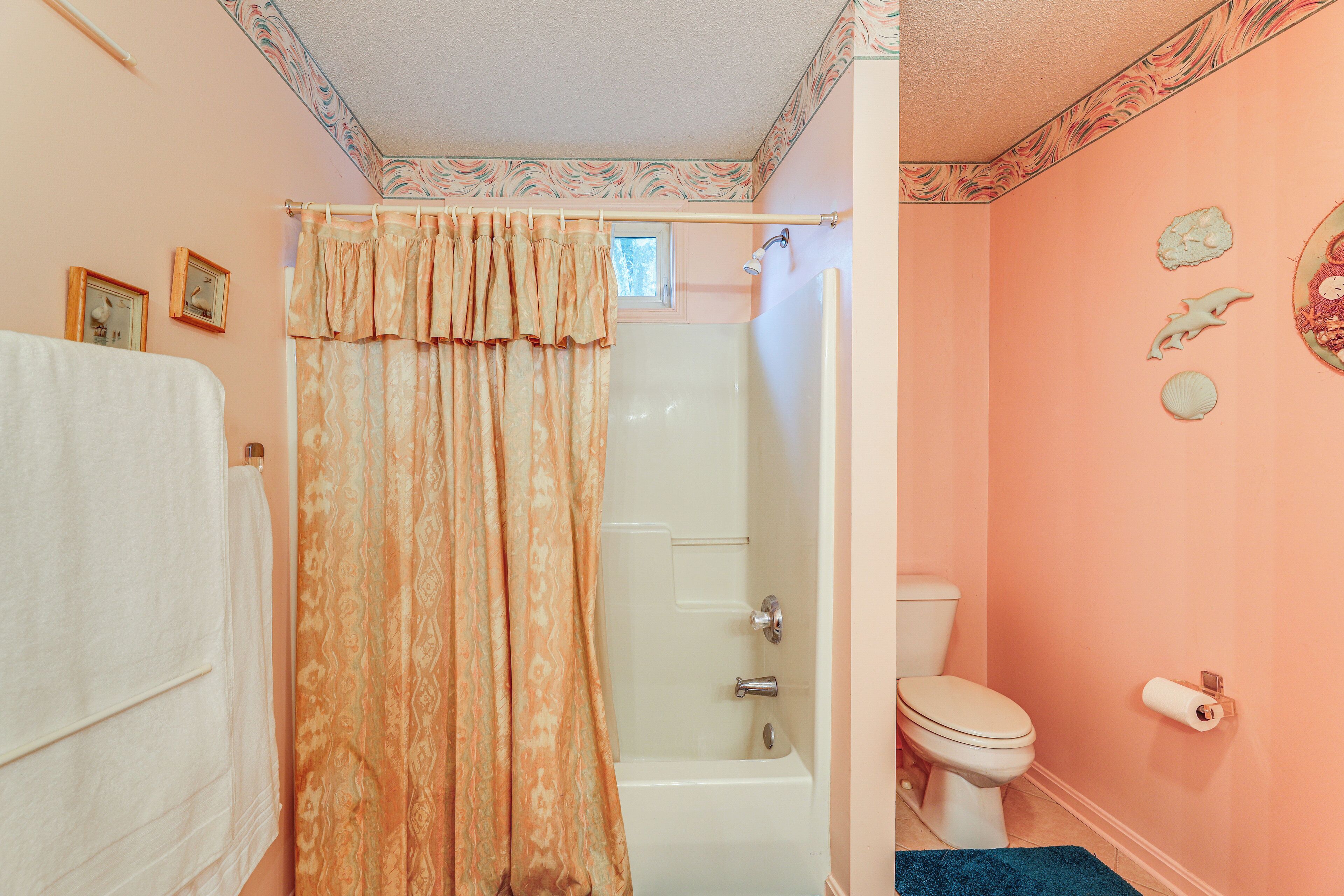 A bathroom with a shower curtain, a bathtub, a toilet, and decorative wall art.