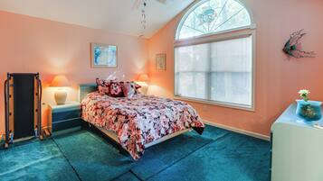 A bedroom with a bed, a desk, a chair, a ceiling fan, a window, and a wall decoration.