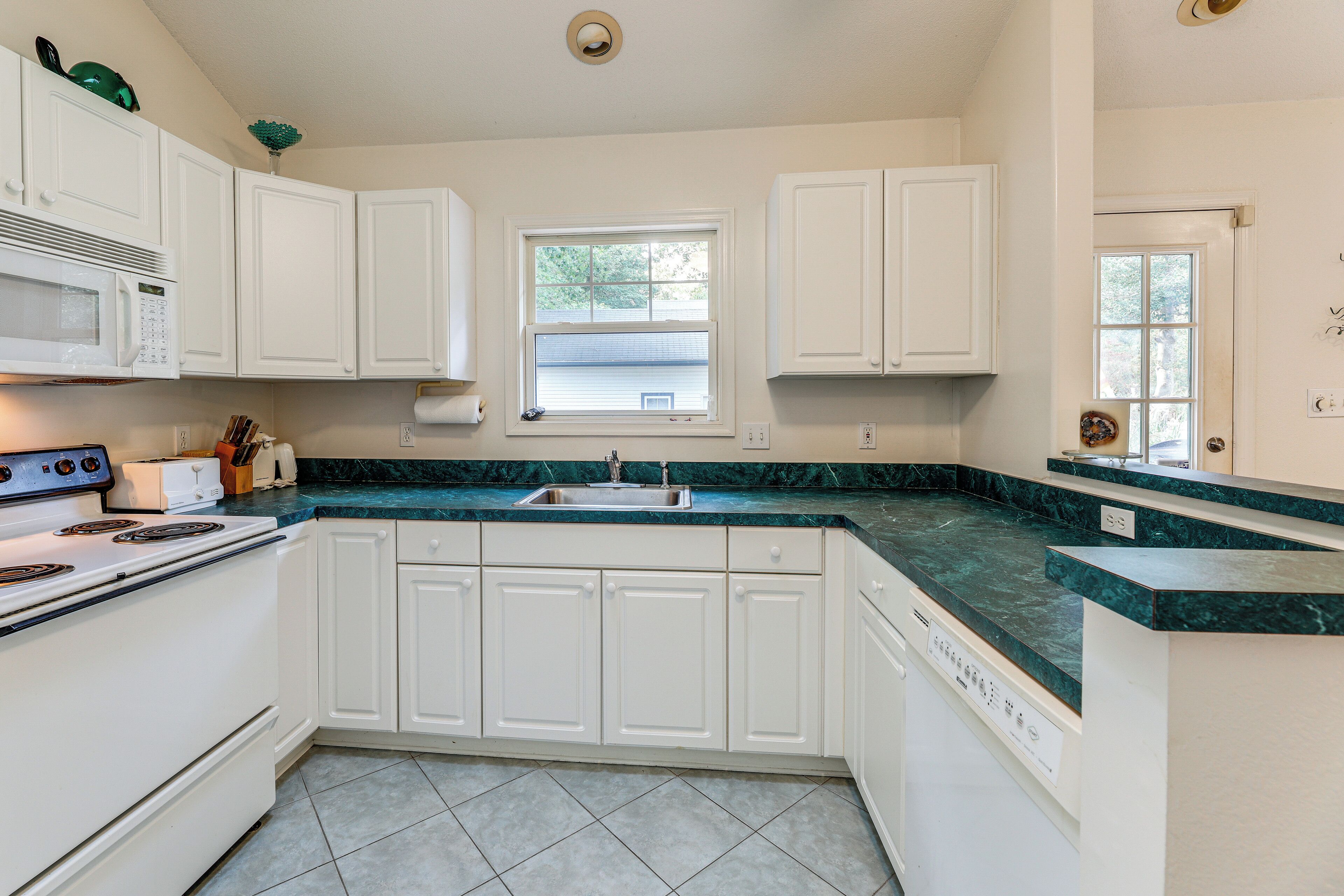 A kitchen with white cabinets, a green marble countertop, a built-in microwave, and a dishwasher.
