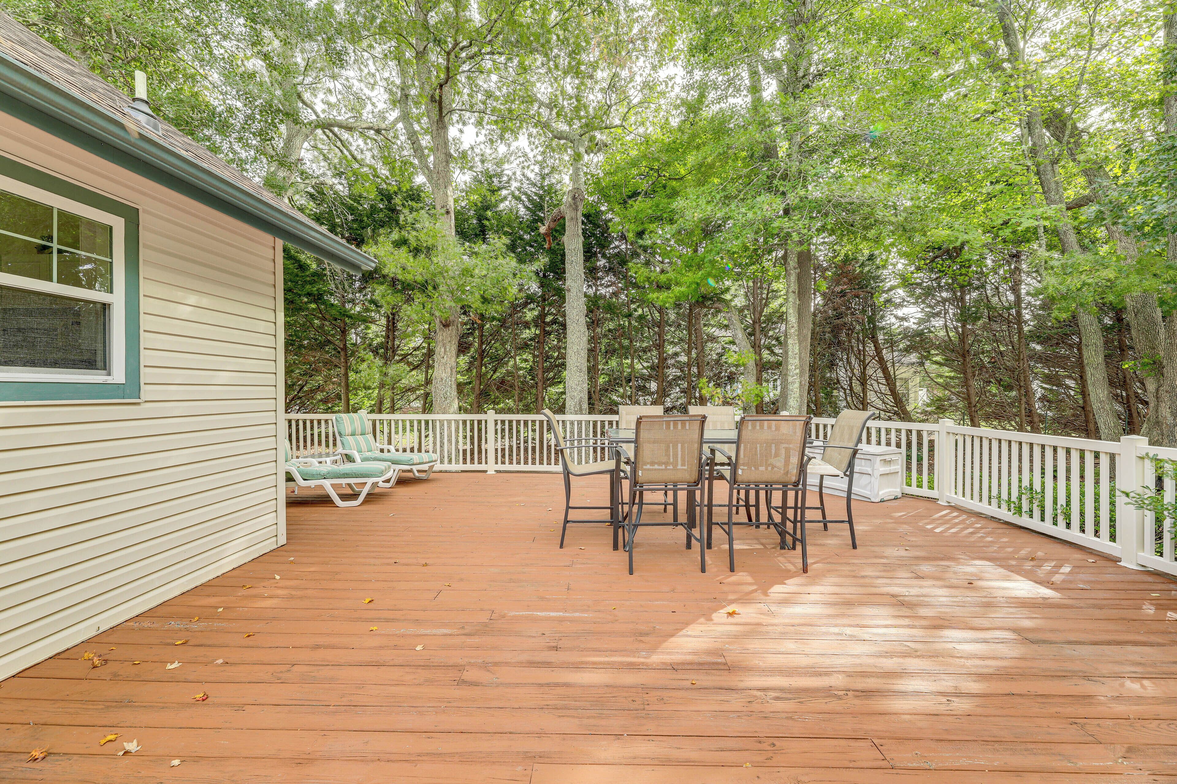 Une terrasse en bois avec une balustrade blanche, entourée d’arbres.