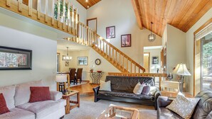 A spacious living area with a wooden staircase, leather sofas, and a dining area with a chandelier. - Private Hot Tub & Sharc Passes! Sunriver Home (Bend)