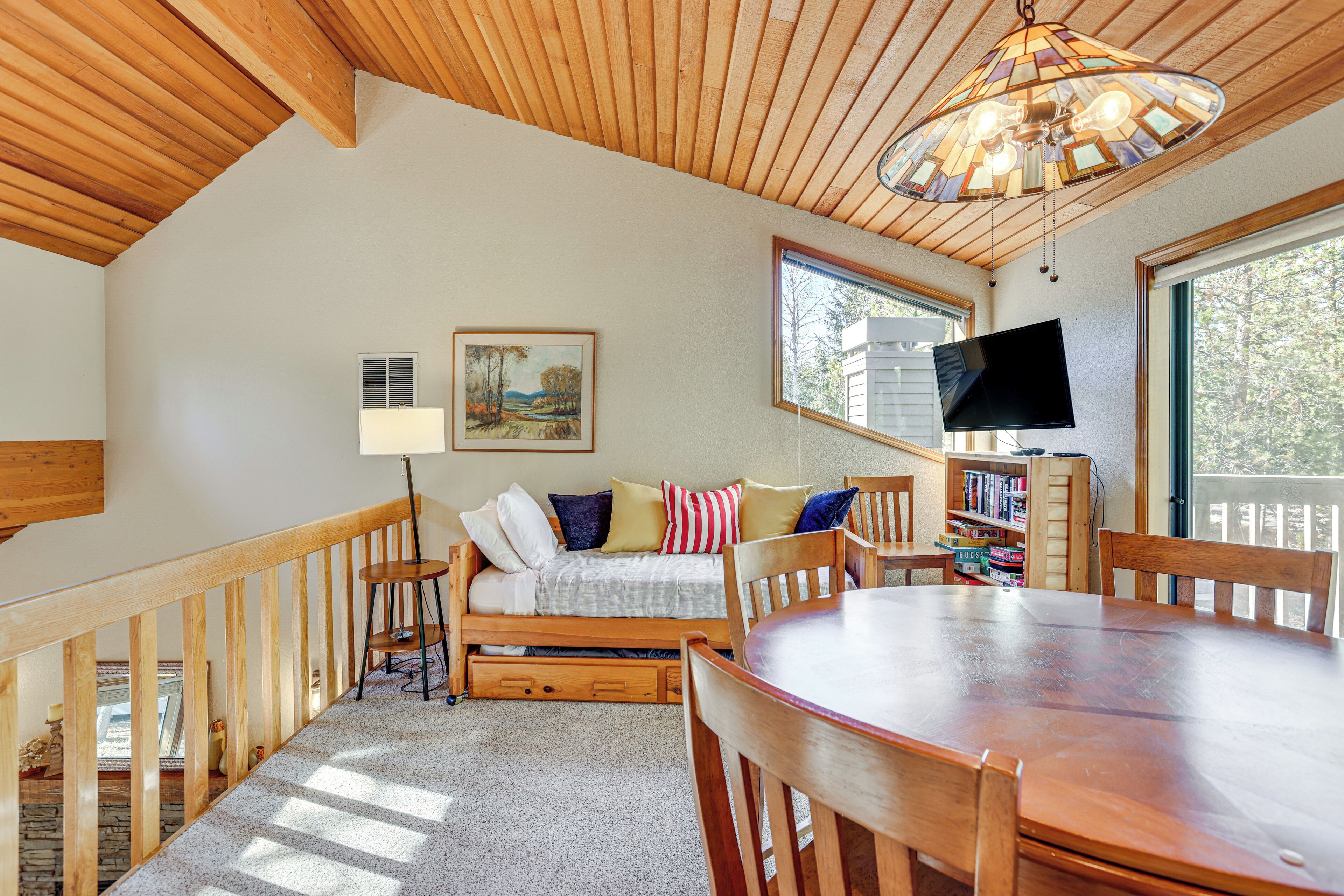 A cozy room with a wooden ceiling, a bed, a dining table, and a TV.