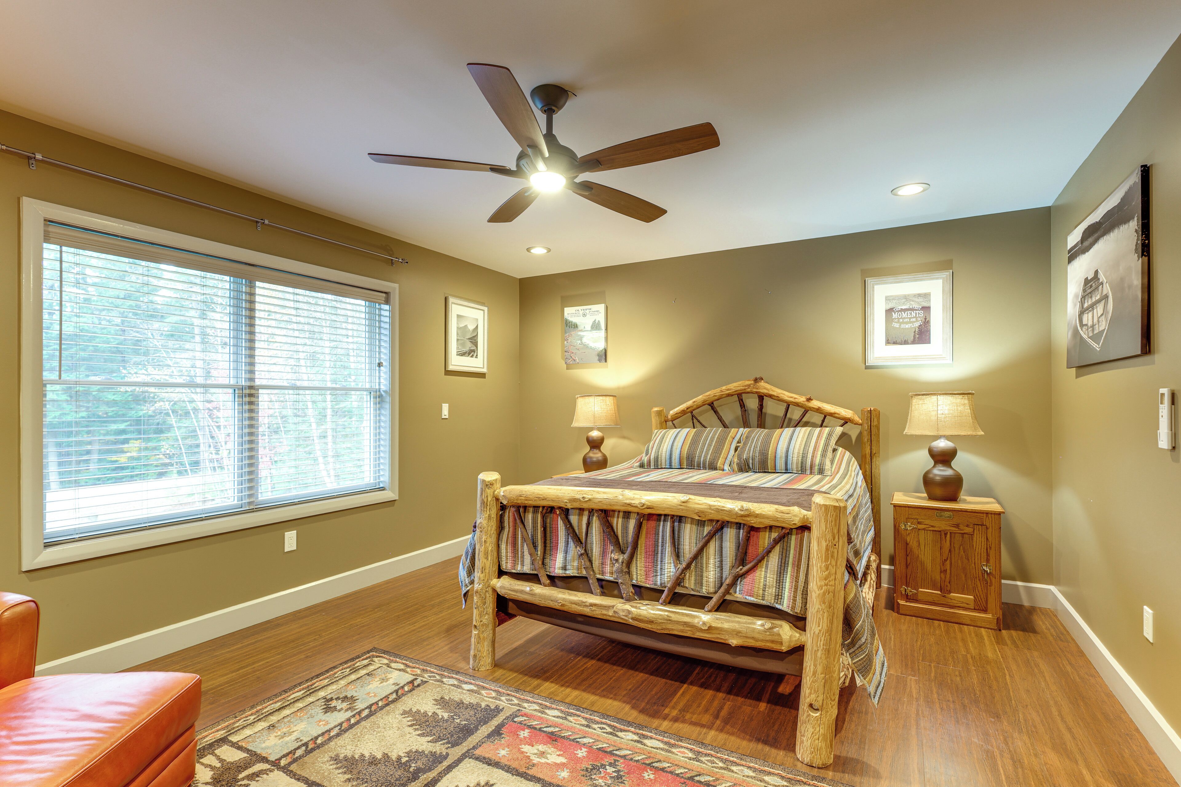 A bedroom with a wooden bed, a ceiling fan, a window with blinds, and a nightstand with a lamp.