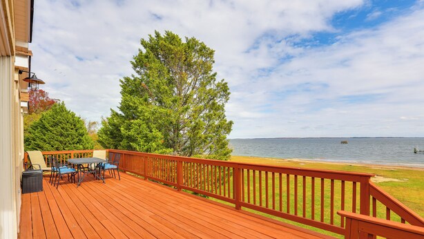 Una terraza de madera con mobiliario exterior, baranda y vista al agua.