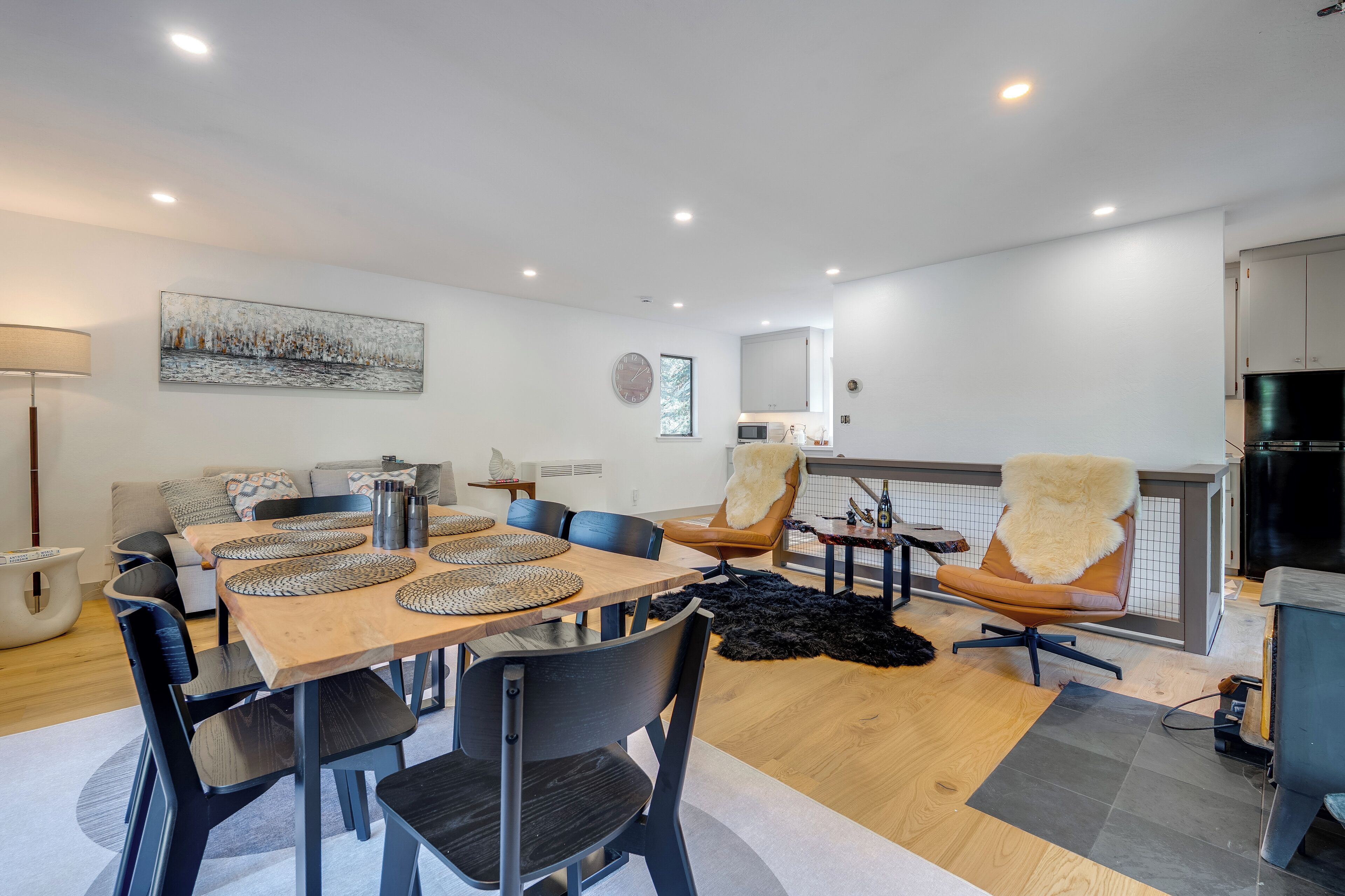 A modern dining area with a wooden table, black chairs, and a black furry rug.