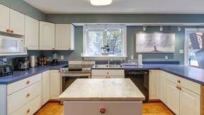 Een moderne keuken met witte kastjes, een marmeren eiland en een groot raam met uitzicht op bomen.