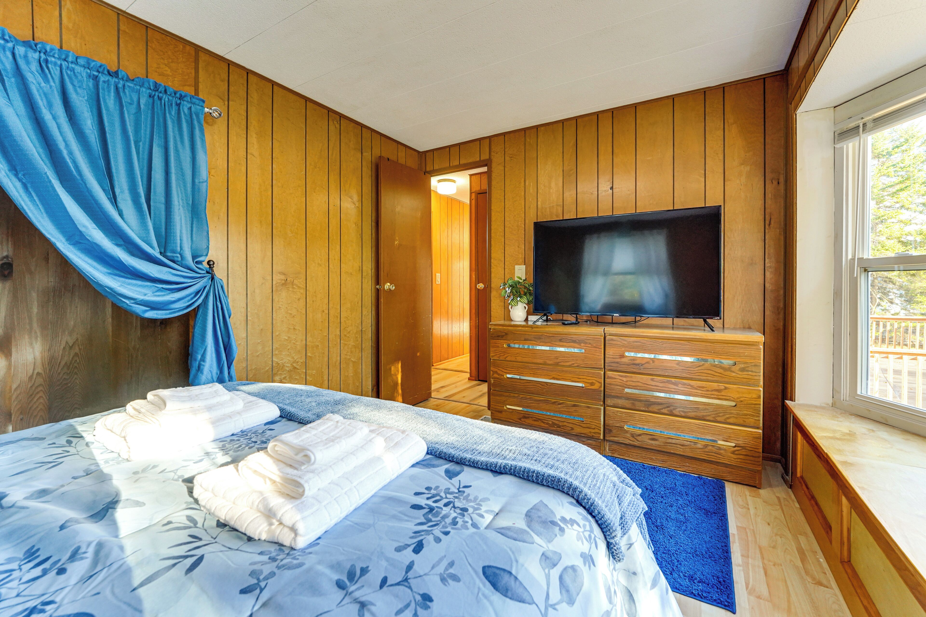 A bedroom with a bed, a TV, wooden walls, a window, and a door.