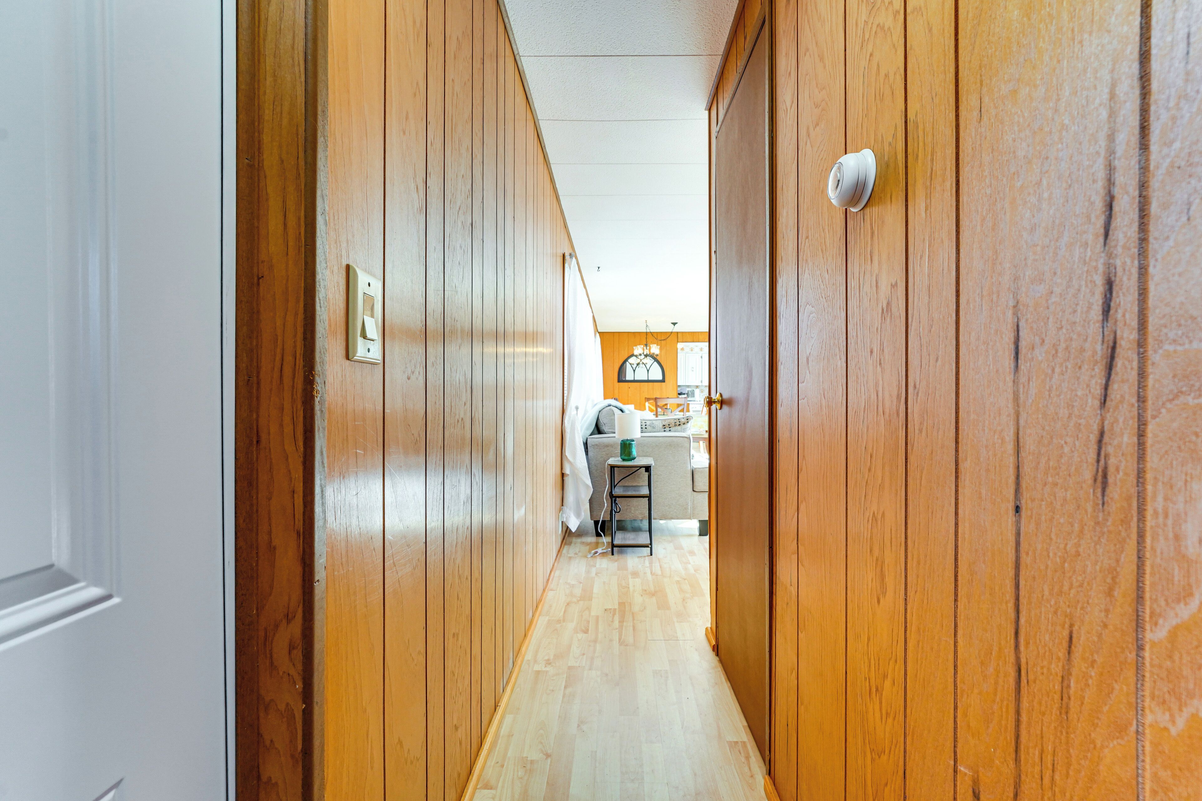 Un pasillo estrecho con paredes de madera y suelo de tono claro, que conduce a una habitación con escritorio y silla.