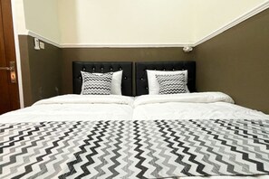 A double bed with a patterned bedspread, two pillows with zigzag patterns, and a dark headboard. - Griya Inn (Tembalang)