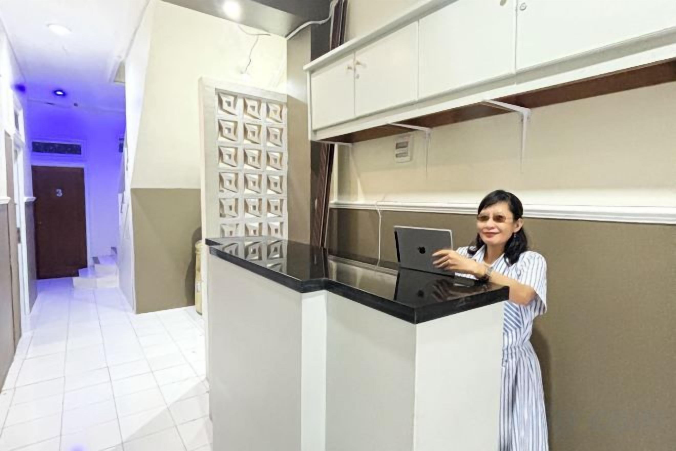 Uma pessoa em pé no balcão de recepção do saguão de um hotel, com balcão e quadro de informações fixado na parede.