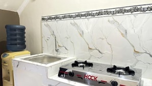 A kitchen with a HOCK gas stove, a sink, and a marble backsplash. - Griya Inn (Tembalang)