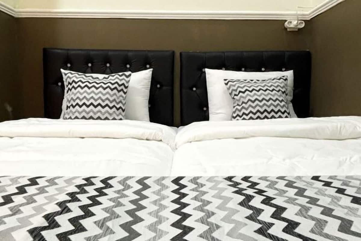 Cama de casal com cabeceira preta e duas almofadas, colcha estampada e parede marrom.