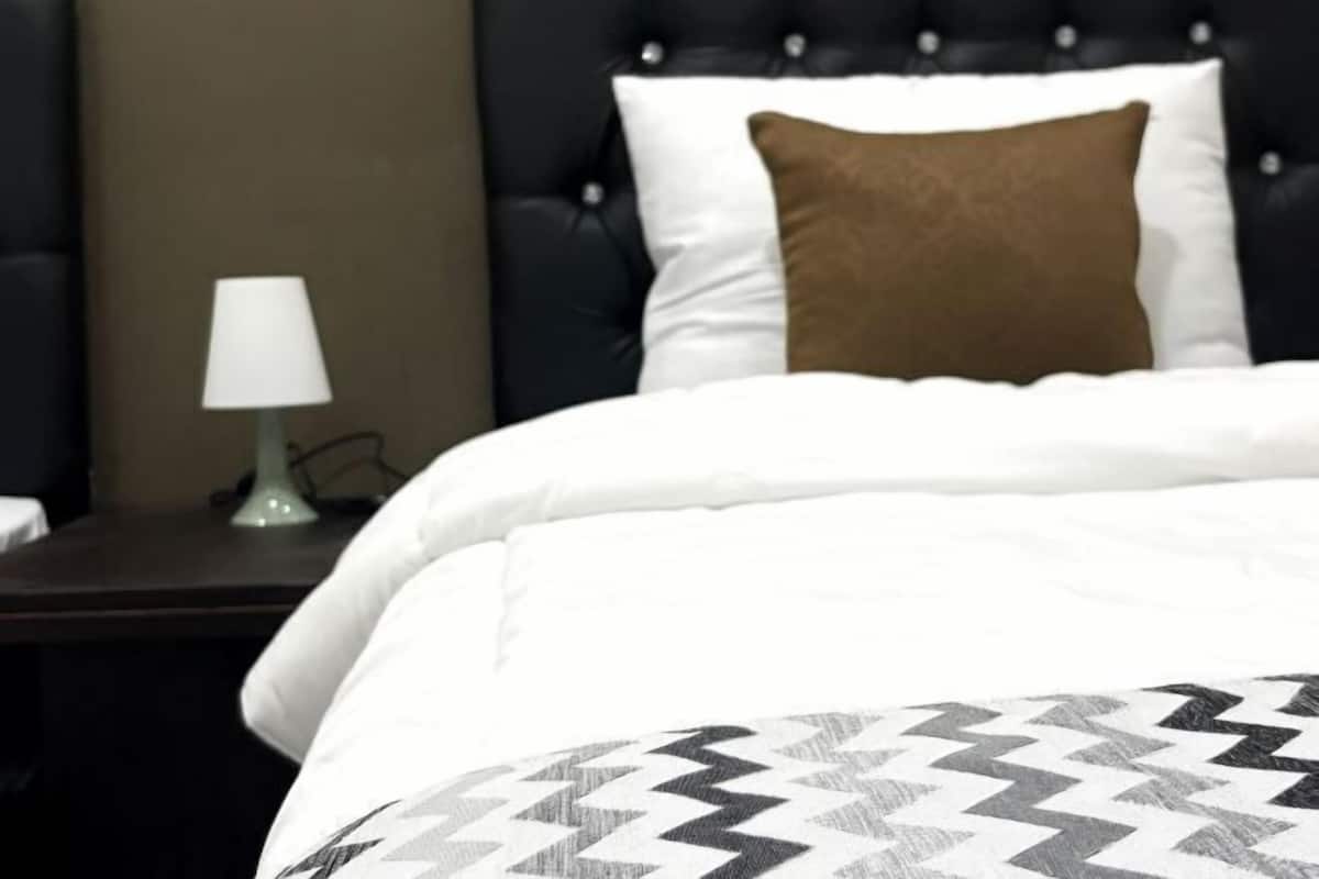 Uma cama com colcha estampada, um travesseiro branco e um travesseiro marrom decorativo.