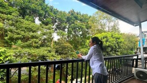 A balcony with a view of lush greenery and a parked car. - Griya Inn (Tembalang)