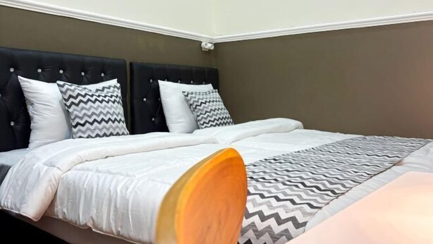 A bed with a black headboard, white bedding, and patterned pillows. - Griya Inn (Tembalang)