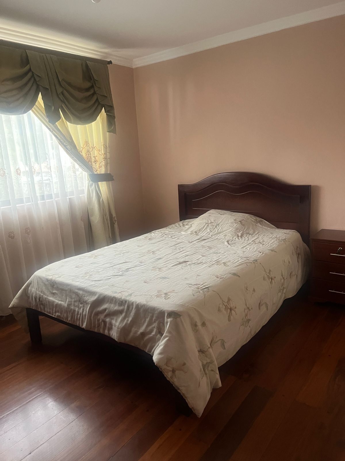 A neatly made bed with a floral bedspread, a wooden headboard, and a nightstand with drawers.