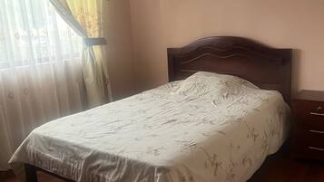 A neatly made bed with a floral bedspread, a wooden headboard, and a nightstand with drawers.