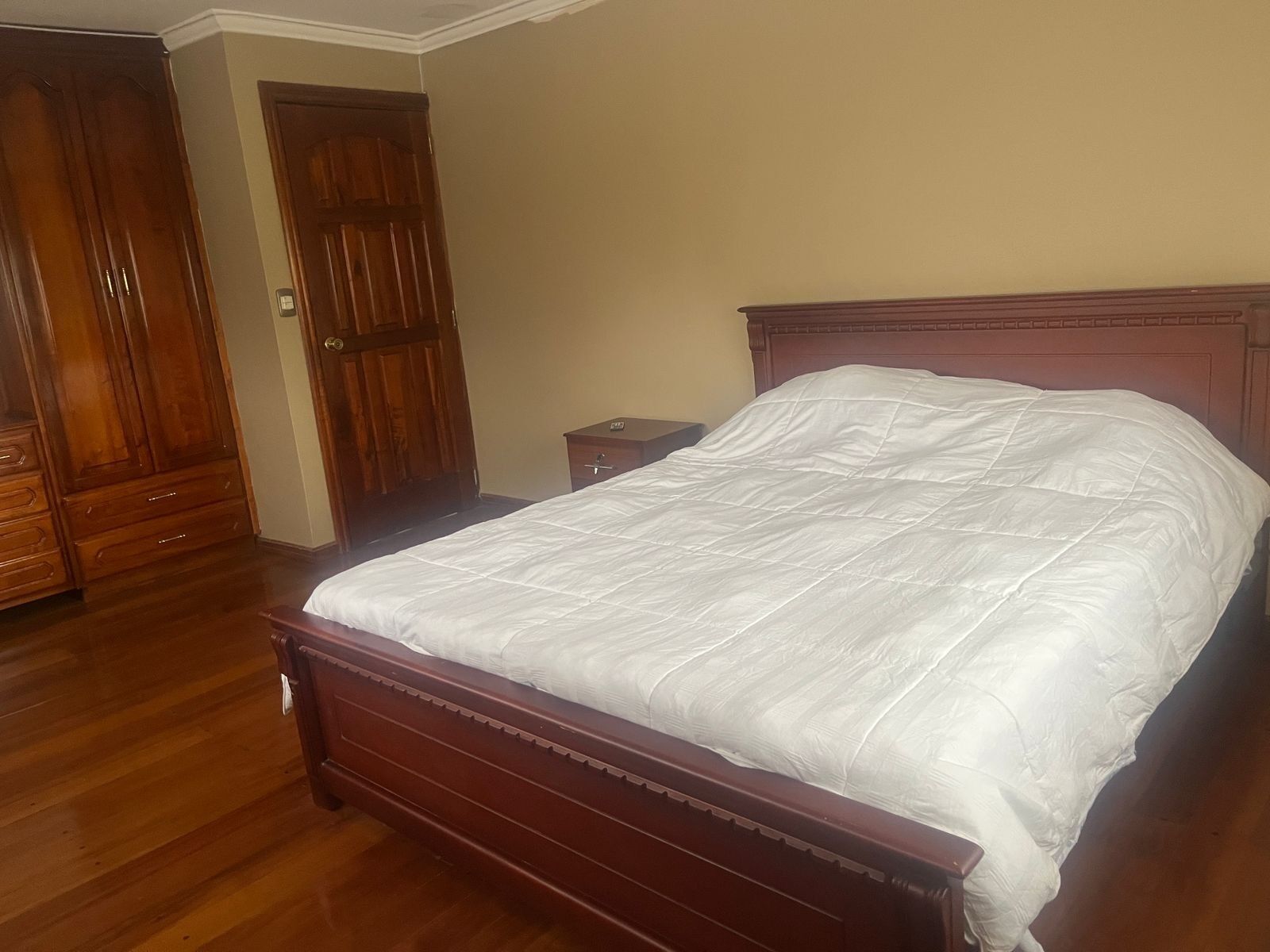 A bedroom with a wooden bed, a nightstand, and a wardrobe.