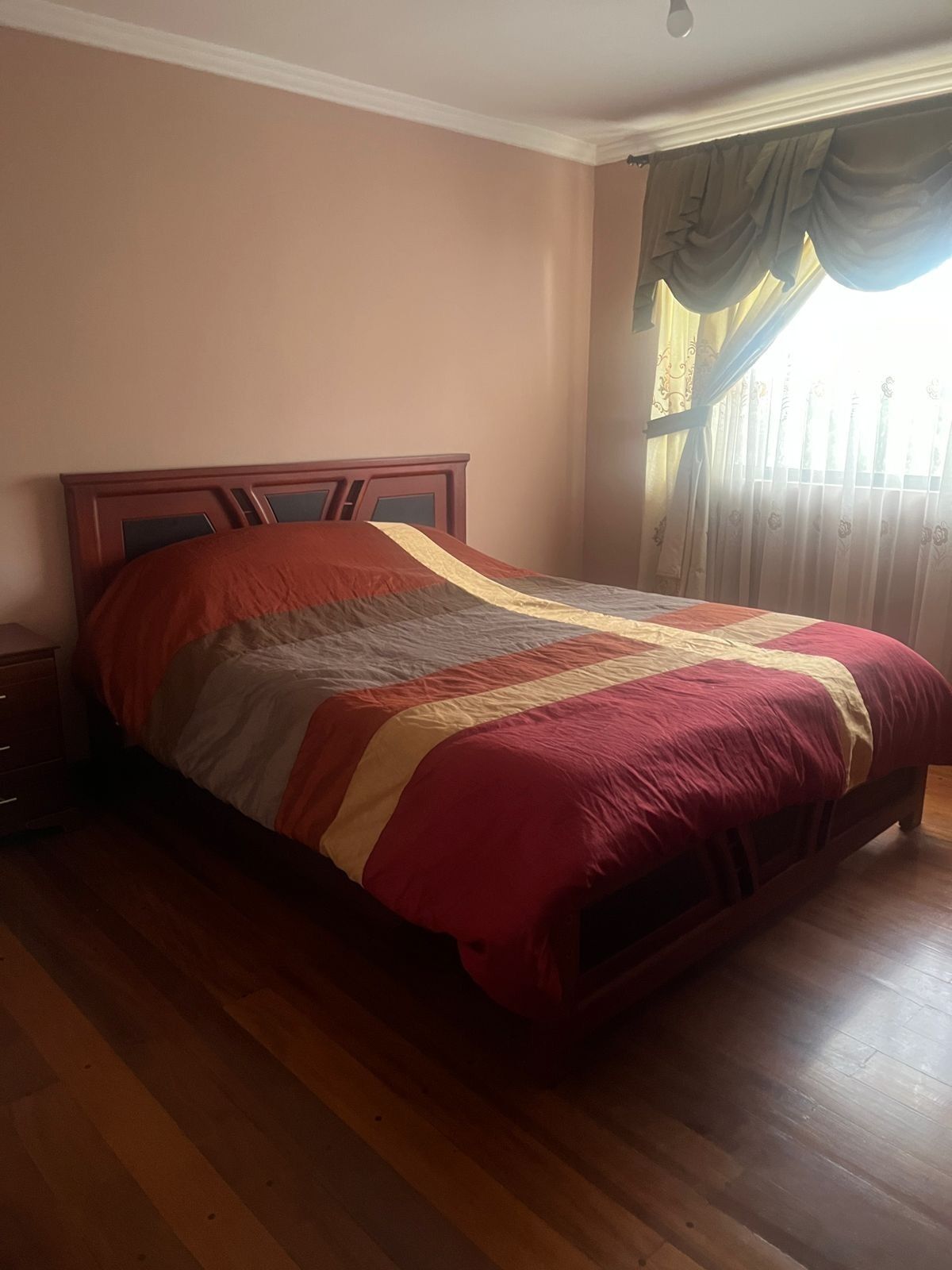 A bedroom with a wooden bed, a nightstand, and a window with curtains.