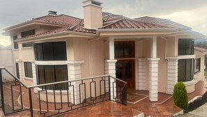 A two-story house with a tiled roof, a balcony, and a staircase leading to the entrance.