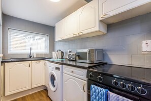 Een kleine keuken met witte kastjes, een wasmachine, een magnetron en een oven.