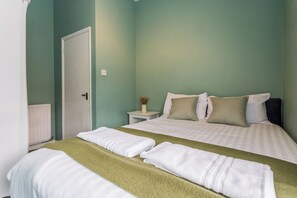 A bedroom with a bed, two pillows, a nightstand with a vase, and a door. - Toast Stays - The Northern View (Sherburn Hill)