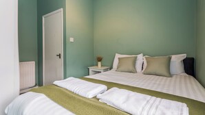Quarto com uma cama, duas almofadas, mesa de cabeceira com um vaso e uma porta.