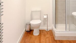 Une salle de bain comprenant des toilettes, une petite poubelle, une cabine de douche en verre et un lavabo blanc.