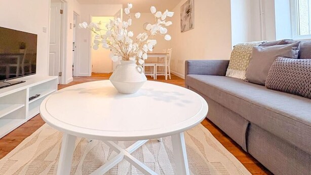 Un salon moderne avec une table ronde blanche, un canapé gris et un vase blanc contenant des fleurs séchées.