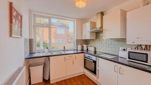 Une cuisine moderne avec des meubles blancs, un plan de travail noir et une fenêtre donnant sur un immeuble en briques.