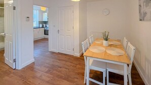 Un coin repas avec une table en bois et des chaises blanches, un luminaire suspendu et une horloge au mur.