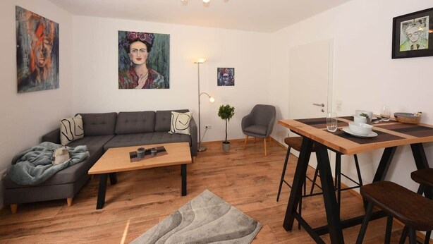 Ett modernt vardagsrum med en grå soffa, ett träbord som används som soffbord och en matplats med ett träbord och stolar.